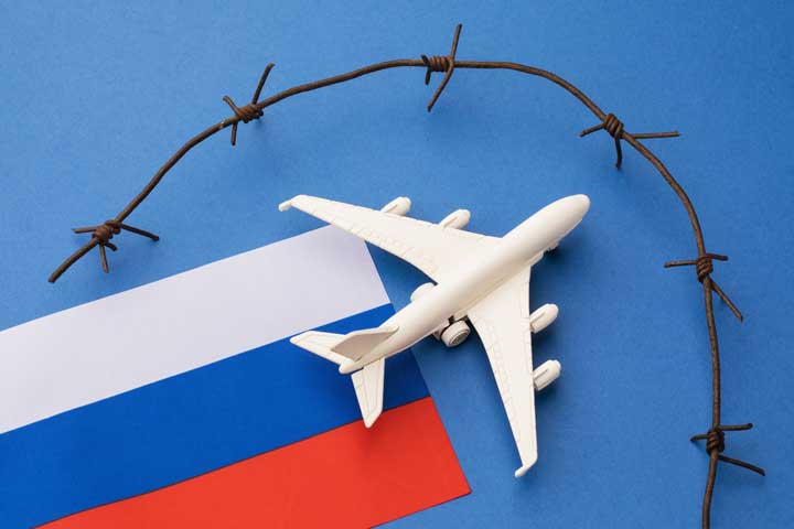 Weißes Flugzeugmodell auf russischer Flagge mit blau-weiß-roten Streifen, umgeben von Stacheldraht, symbolisiert die Grenzen der Rechtsberatung aufgrund der Russlandsanktionen