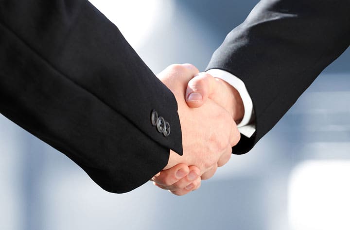 Nahaufnahme von zwei Personen in schwarzen Anzügen beim Handschlag – symbolisiert Vereinbarung oder Partnerschaft im Kontext eines Deals mit der Finanzstrafbehörde