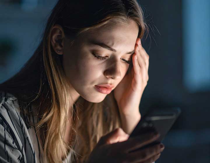 Frau liest besorgt Hasskommentare und Beleidigungen auf dem Smartphone – Schutz der Persönlichkeitsrechte im Internet