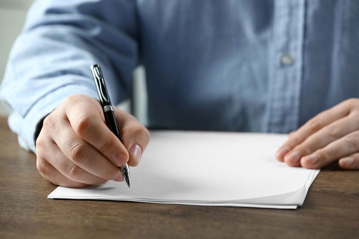 Eine Person schreibt mit einem Stift auf ein Blatt Papier